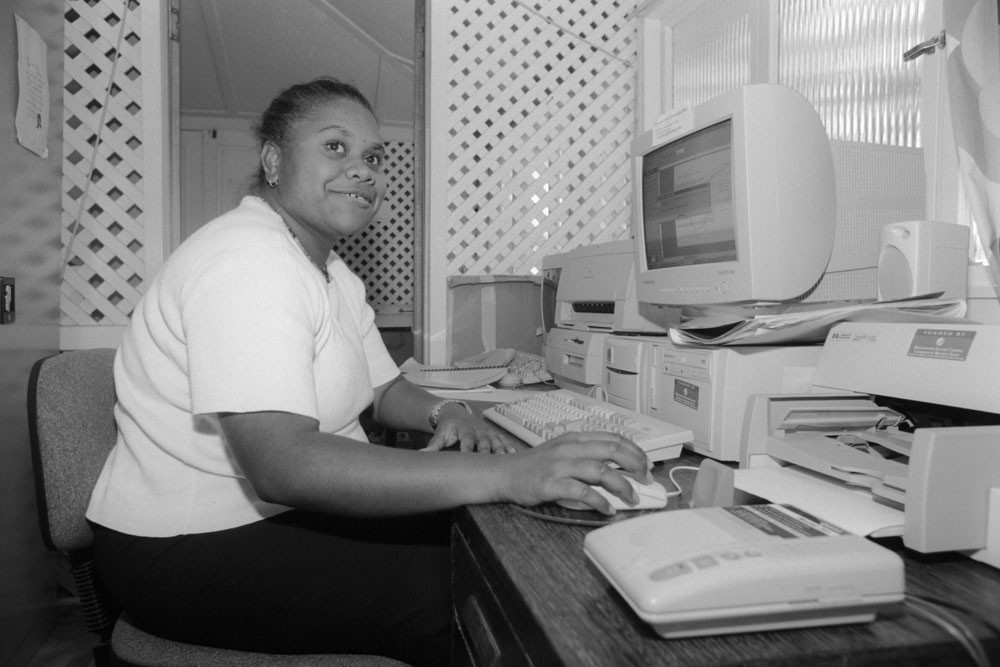 Woman in a white shirt, using a computer inside the Mackay and District Australian South Sea Islander Association office